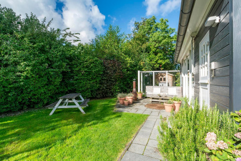 Hyggelig have ved lodge Eureka 109 i Holland, med grøn plæne, bænk og terrasseterrasse i solen.
