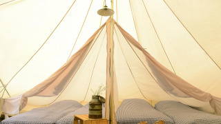 Interior of Tipitent de Jutter teepee tent with three single beds, checked sheets and rustic decor.