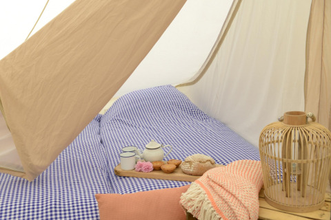 Intérieur de tipi cosy avec draps à carreaux bleus, plateau de thé et lanterne au Tipitent de Jutter.