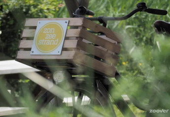 Cykel med trækasse og skiltet 'zon zee strand' foran tipiteltet de Jutter i Holland, omgivet af grønt.