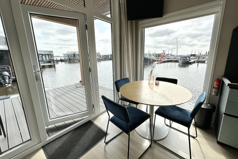 Indendørs spiseplads med udsigt over vandet fra husbåden RiggelBrug Sneekermeer i Holland.