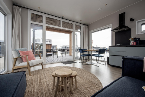 Moderne stue på husbåd 'RiggelBrug Sneekermeer' i Nederlandene med udsigt over vandet og terrasse.