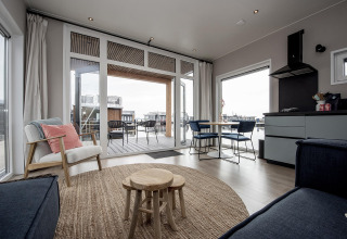 Moderne stue på husbåd 'RiggelBrug Sneekermeer' i Nederlandene med udsigt over vandet og terrasse.