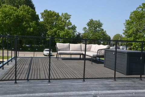Tagterrasse på husbåd med sofasæt og sort rækværk, omgivet af træer ved Sneekermeer i Holland.