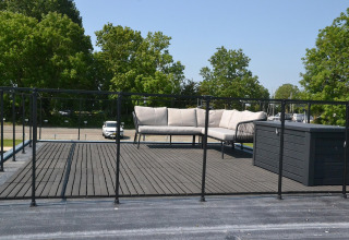Tagterrasse på husbåd med sofasæt og sort rækværk, omgivet af træer ved Sneekermeer i Holland.