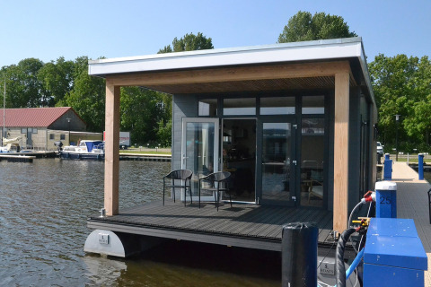 Moderne husbåd ved vandet, 'RiggelBrug Sneekermeer', med terrasse i Holland på en solskinsdag.