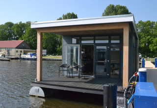 Moderne husbåd ved vandet, 'RiggelBrug Sneekermeer', med terrasse i Holland på en solskinsdag.