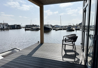 Udsigt fra en husbåd ved navn 'RiggelBrug Sneekermeer' med både og terrassestol i Holland.