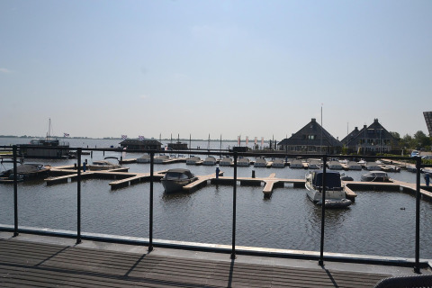 Udsigt fra husbåden RiggelBrug Sneekermeer over en marina med både og hytter ved vandet i Holland.