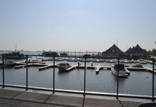 Udsigt fra husbåden RiggelBrug Sneekermeer over en marina med både og hytter ved vandet i Holland.