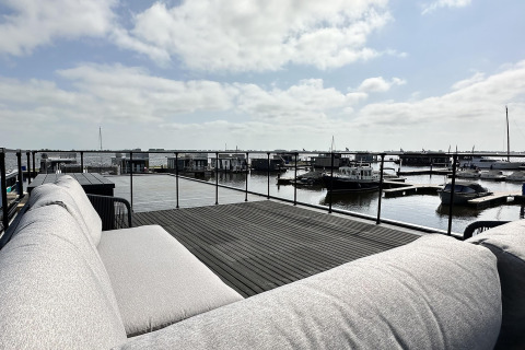 Udsigt fra en husbåd ved RiggelBrug Sneekermeer med sofa, terrasse og både i havnen, Holland.