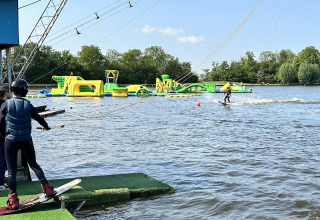 Wakeboardere gør sig klar ved søen nær en stor oppustelig forhindringsbane i det fri.