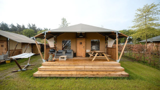 Tenda safari Villatent Cottage con veranda in legno, arredi da esterno e amaca in uno spazio verde.