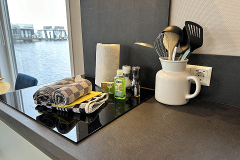 Moderne køkkenbord på husbåd med udsigt over vandet, viskestykker, køkkenrulle og køkkenredskaber.