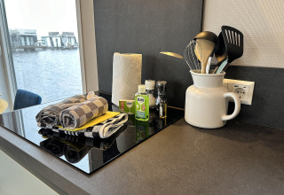 Moderne køkkenbord på husbåd med udsigt over vandet, viskestykker, køkkenrulle og køkkenredskaber.