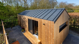 Modern tiny house met houten gevelbekleding en zwart dak, gelegen in een groene en bosrijke tuin.