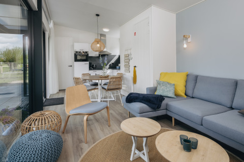 Moderne lodgeinteriør med lyst træ, blå sofa og spiseplads ved Park Wijdenes 4 i Holland.