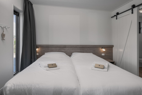 Moderne dobbeltseng i Park Wijdenes 4 lodge, Holland, med hvide lagner og naturligt lysindfald.
