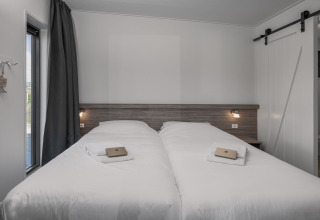 Moderne dobbeltseng i Park Wijdenes 4 lodge, Holland, med hvide lagner og naturligt lysindfald.