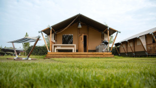Villatent Nomad safari tent with wooden deck, bench, and barbecue on a grassy lawn under a blue sky.