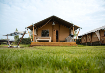 Villatent Nomad safari tent with wooden deck, bench, and barbecue on a grassy lawn under a blue sky.