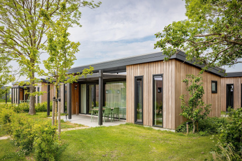 Et moderne træbeklædt lodge ved Park Wijdenes i Holland, omgivet af grønne træer og velplejede buske.