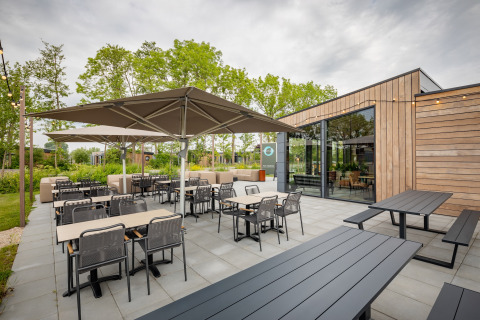 Udendørs spiseområde ved en moderne lodge med parasoller, borde og stole omgivet af grønne planter.