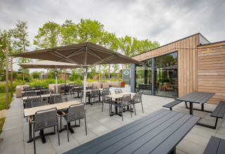 Udendørs spiseområde ved en moderne lodge med parasoller, borde og stole omgivet af grønne planter.