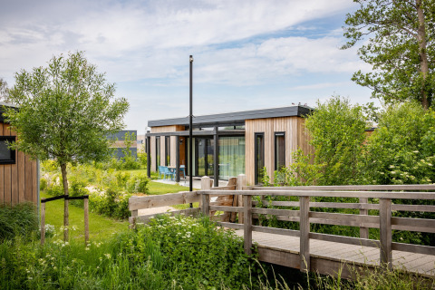 Moderne feriebolig Park Wijdenes 4 med træfacade i Holland, omgivet af grønne planter og træer.
