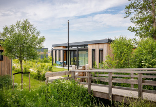 Moderne feriebolig Park Wijdenes 4 med træfacade i Holland, omgivet af grønne planter og træer.