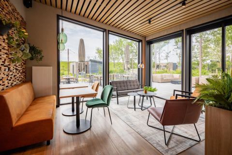 Moderne lodge lounge med store vinduer, komfortable siddepladser og udsigt over en udendørs terrasse.