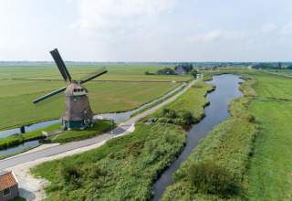 Billede af en traditionel hollandsk vindmølle ved en flod med frodige grønne marker og en blå himmel.