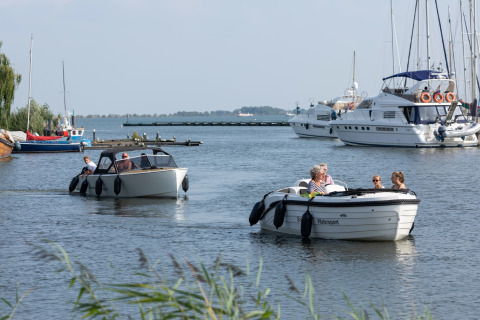 Folk sejler i både ved en lystbådehavn med store yachter og mindre både i baggrunden om dagen.