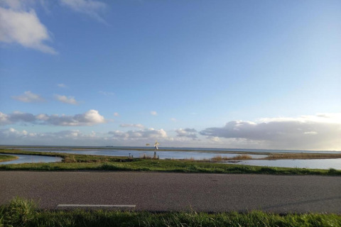 Billede af en landevej, brede marker, en mølle og åbent himmeludsyn taget fra en lodge ved vandet.