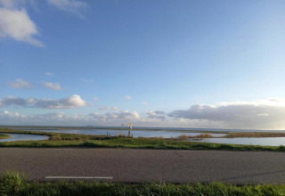 Billede af en landevej, brede marker, en mølle og åbent himmeludsyn taget fra en lodge ved vandet.