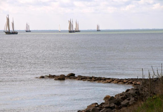 Udsigt over havet med sejlskibe i horisonten set fra en lodge, med stensætning i forgrunden.