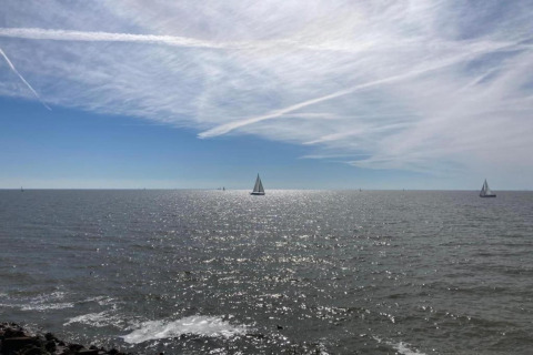 Udsigt til havet med sejlskibe, fredfyldt vand og blå himmel set fra en lodge tæt på kysten.