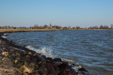 Billede af en kystnær lodge med stenstrand, bølger og udsigt til en landsby med en kirke i baggrunden.