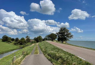 Landskabsbillede af en landevej ved siden af havet med grønne marker, træer og blå himmel med skyer.