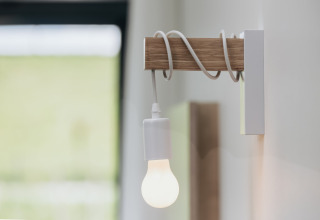 En moderne lampe med træarm og snoet ledning monteret på væggen i et lodge-værelse med blødt lys.