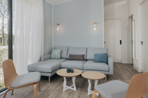 Moderne stue i Park Wijdenes 3, Holland, med lyseblå sofa, træmøbler og store vinduer.