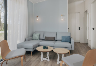 Moderne stue i Park Wijdenes 3, Holland, med lyseblå sofa, træmøbler og store vinduer.