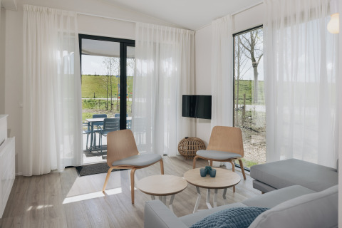 Lyst og moderne opholdsstue i Park Wijdenes 3 lodge i Holland med udsigt til terrasse og grønt område.