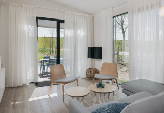 Lyst og moderne opholdsstue i Park Wijdenes 3 lodge i Holland med udsigt til terrasse og grønt område.