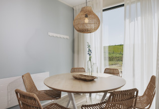 Spisestue med runde bord, fletstole og hængende lampe i Park Wijdenes 3-lodge i Holland med udsigt.