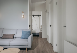 Moderne stue i Park Wijdenes 3, Holland, med lys sofa, træbord og adgang til soveværelse.