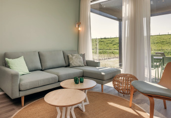 Lyst, moderne stue i Park Wijdenes 2 med grå sofa, runde borde og udsigt til grønt landskab i Holland.