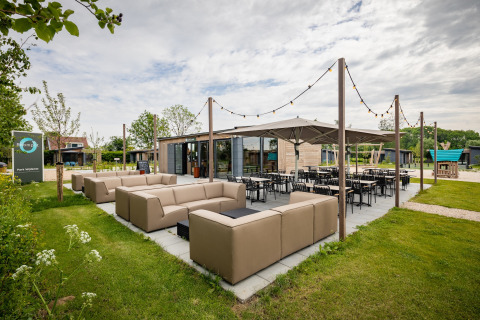 Udendørs siddeområde ved en moderne lodge med komfortable sofaer, borde og lyskæder under åben himmel.