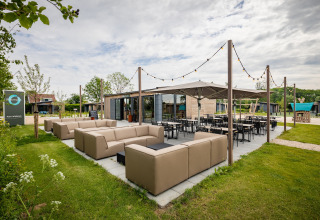 Udendørs siddeområde ved en moderne lodge med komfortable sofaer, borde og lyskæder under åben himmel.