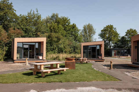 Contemporary wooden tiny houses at Noordzee Résidence De Banjaard with picnic tables on green lawn.